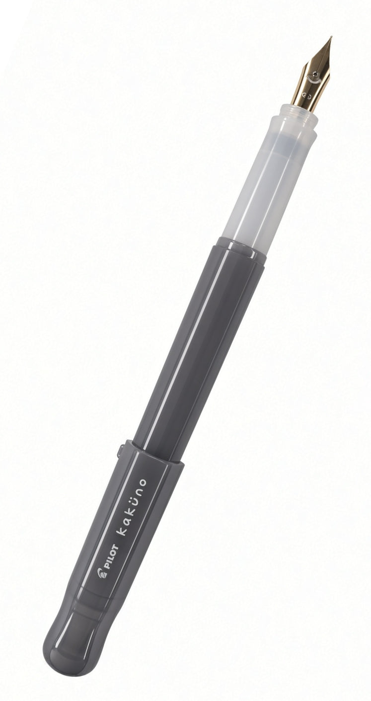 The Pilot Kakuno Fountain Pen features a gray barrel with the “kaküno” label, smiley face, and Pilot branding. It has a transparent grip section and a gold nib, is compatible with standard fountain pen cartridges, and is displayed against a white background.