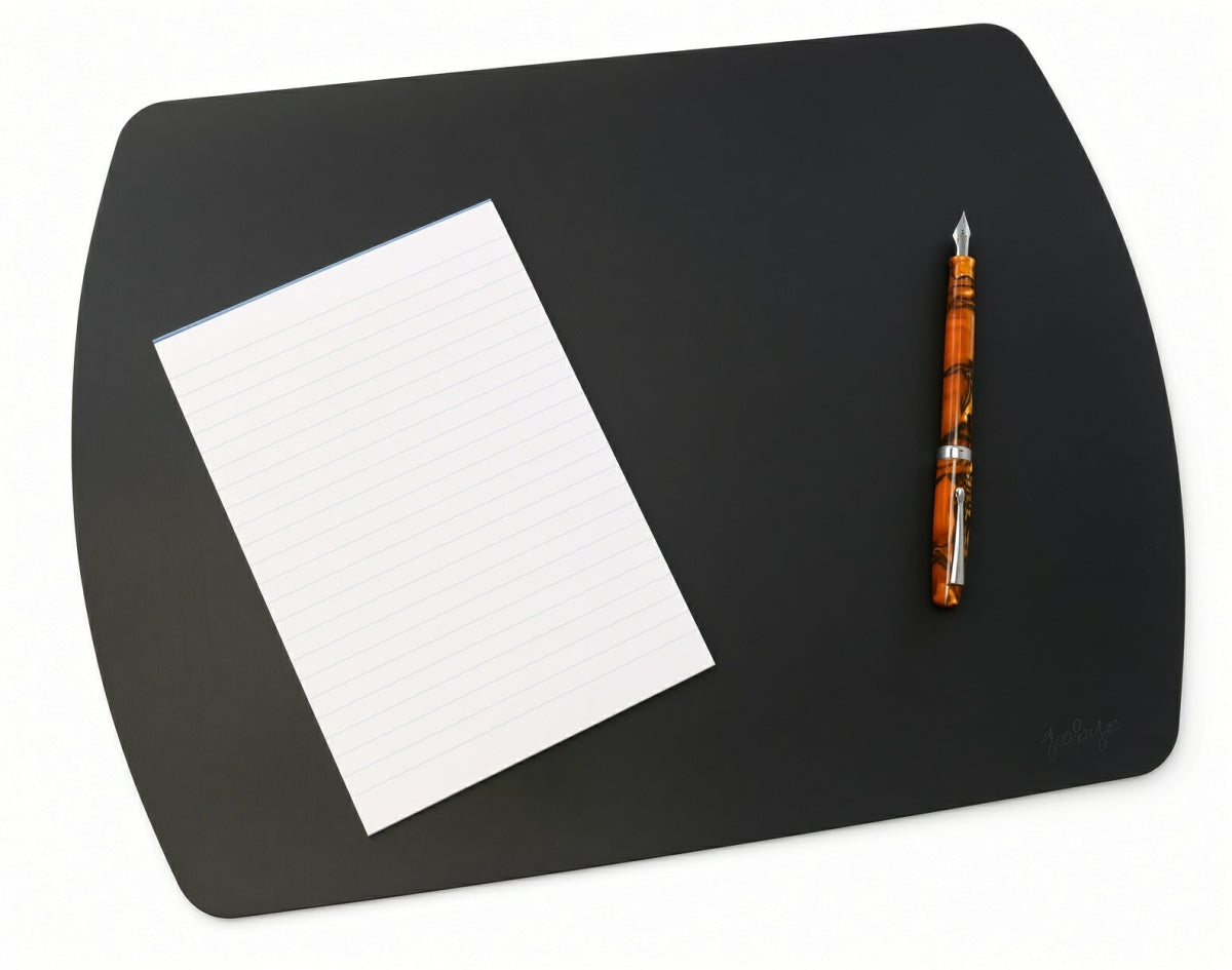 A black Girologio Writing Mat - Black with rounded corners, featuring a lined notepad and an orange marbled fountain pen, providing stylish desk protection.