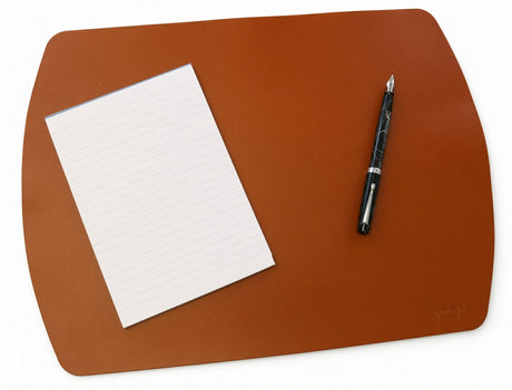 A brown rectangular Girologio Writing Mat - Cognac with rounded corners, featuring a blank lined notepad and a fountain pen placed on its surface.