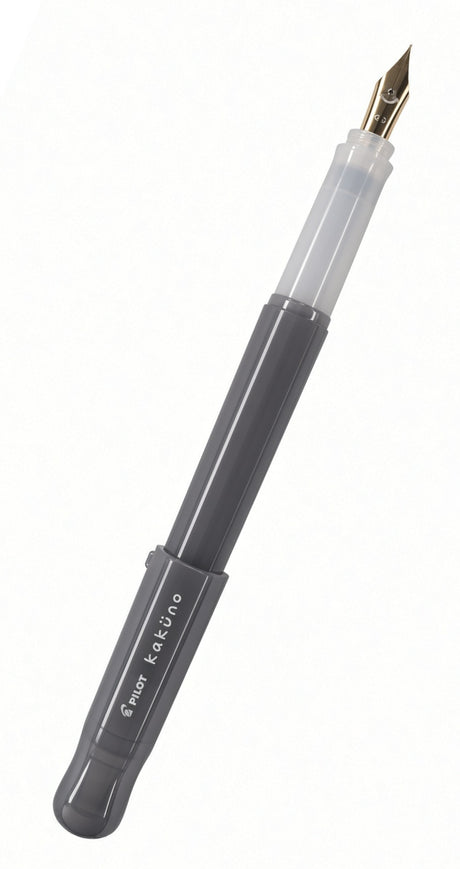 The Pilot Kakuno Fountain Pen features a gray barrel with the “kaküno” label, smiley face, and Pilot branding. It has a transparent grip section and a gold nib, is compatible with standard fountain pen cartridges, and is displayed against a white background.