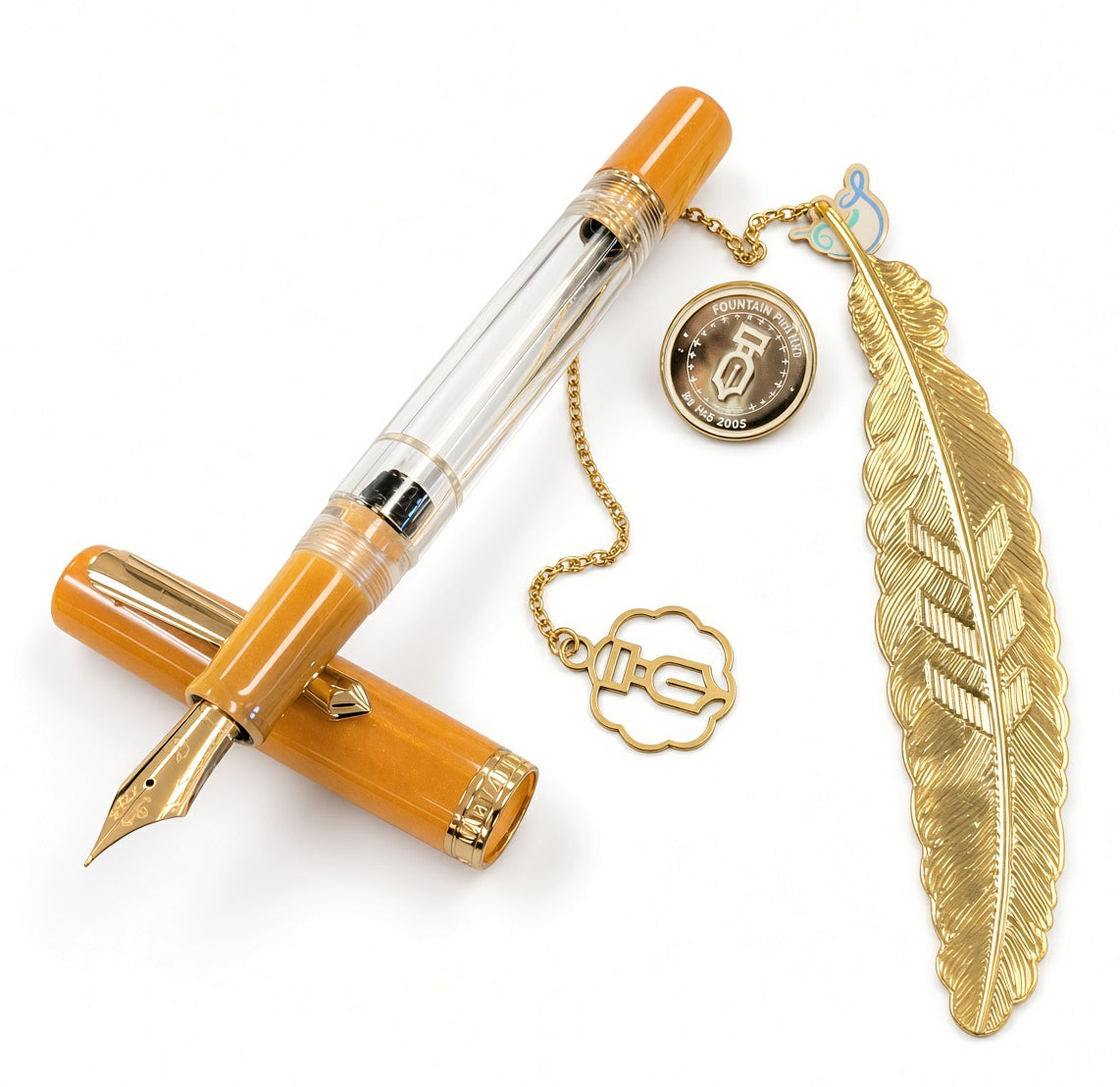 Mustard yellow Italian acrylic Nahvalur Original Plus Fountain Pen - Fountain Pen Day 2026 (Limited Edition) with a transparent barrel, a gold-toned feather bookmark on a chain, and a circular metal commemorative coin.