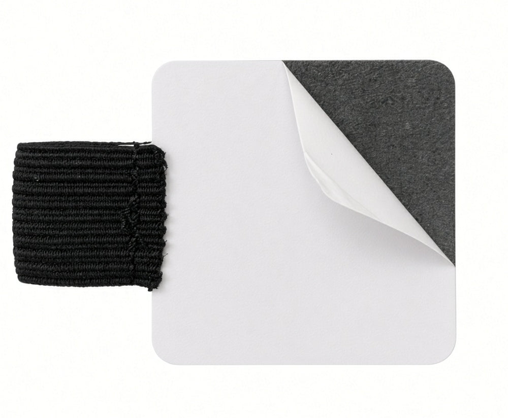 A square white FPR Pen Loop - self-adhesive pen notebook holder features one corner partially peeled to reveal a dark backing. Affixed to the patch’s left side is a short, thick black elastic pen loop—making it an ideal adhesive pen holder and practical journal accessory for keeping your favorite writing tool always within reach.