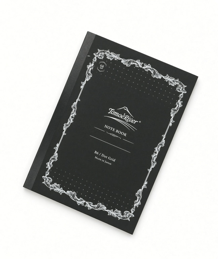 Tomoe River B6 Notebook - Dot Grid (68gsm) with a black cover, white ornate border, and NOTE BOOK printed on the front; this fountain pen friendly, dot grid stationery is ideal for detailed journaling.