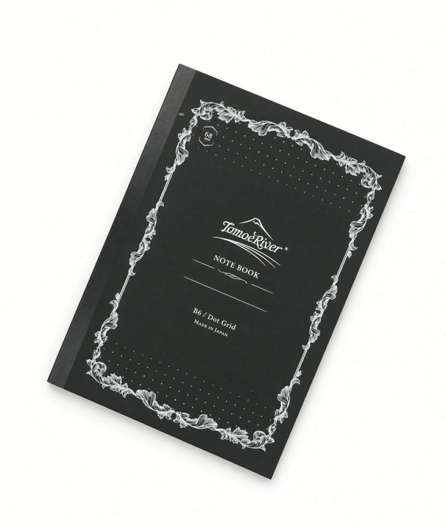 Tomoe River B6 Notebook - Dot Grid (68gsm) with a black cover, white ornate border, and NOTE BOOK printed on the front; this fountain pen friendly, dot grid stationery is ideal for detailed journaling.